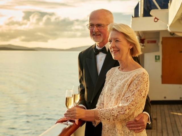 A couple on the Promenade Deck on the Hebridean Princess cruise ship of Hebridean Island Cruises with glasses of champagne